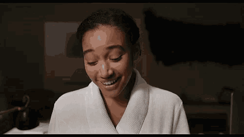a woman in a white bathrobe is smiling in a dark room .