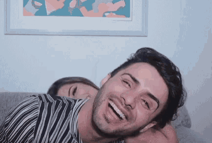 a man and woman are laying on a couch and laughing .