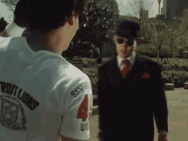 a man in a suit and sunglasses stands next to a man in a white shirt that says lions