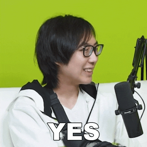 a man wearing glasses is smiling in front of a microphone and the word yes is visible