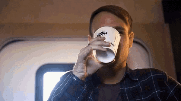 a man in a plaid shirt is drinking from a paper cup that says ' alpine ' on it