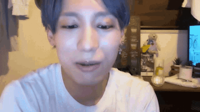 a man with blue hair is wearing a white shirt and looking at the camera .