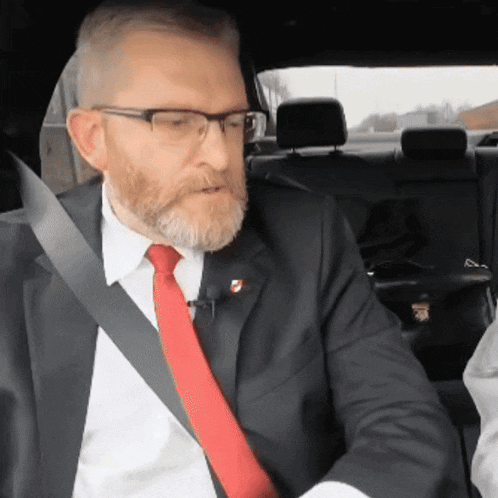 a man with glasses and a red tie is sitting in a car