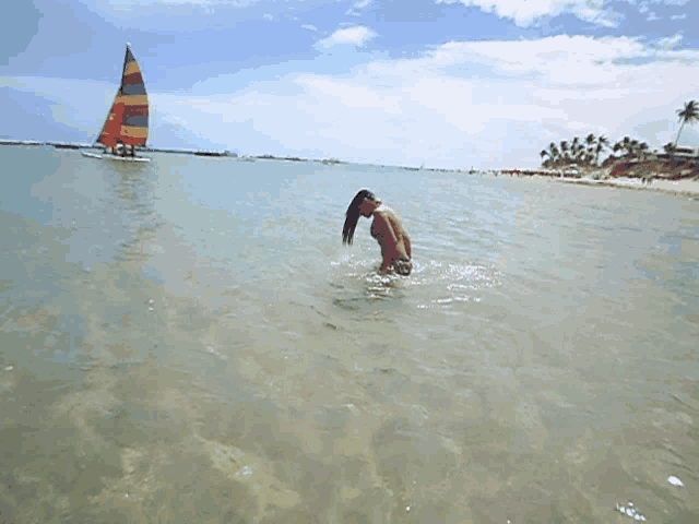 a man is swimming in the ocean with a sailboat behind him
