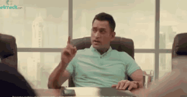 a man in a blue shirt is sitting at a table in a conference room talking to someone .