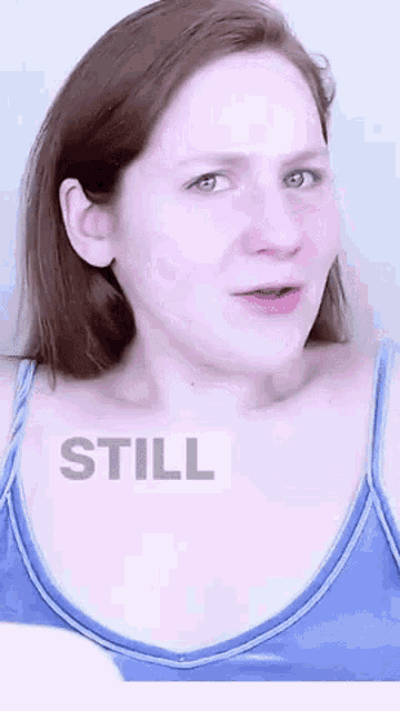 a woman in a blue tank top is making a funny face and has the word still written on her chest .