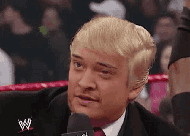 a man in a suit and tie is talking into a microphone while wearing a wig .