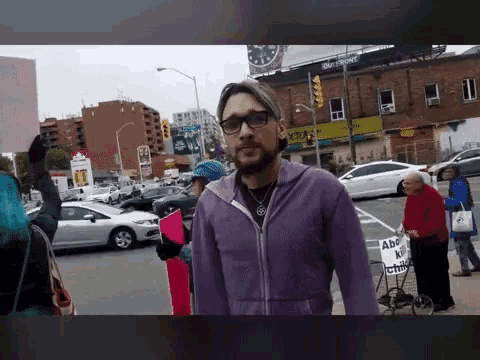 a man in a purple jacket is walking down a street holding a sign that says " abolish capitalism "