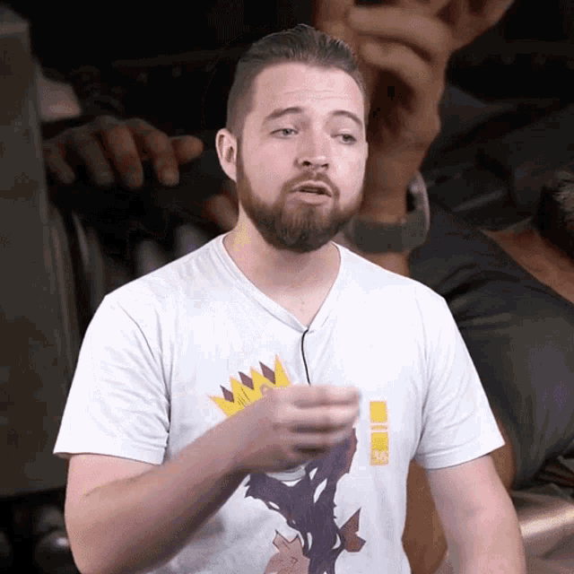 a man with a beard wearing a white t-shirt with a crown on it