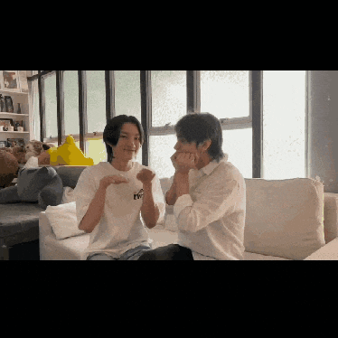 two young men are sitting on a couch with their hands on their faces