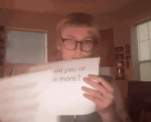 a person wearing glasses holds a piece of paper that says " will you or be more "