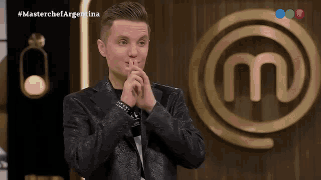 a man in a black jacket stands in front of a masterchef argentina logo