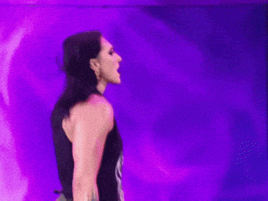 a woman in a black dress is standing in front of a purple wall .
