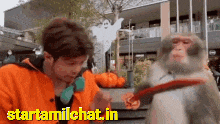 a man in an orange jacket is standing next to a monkey on a leash