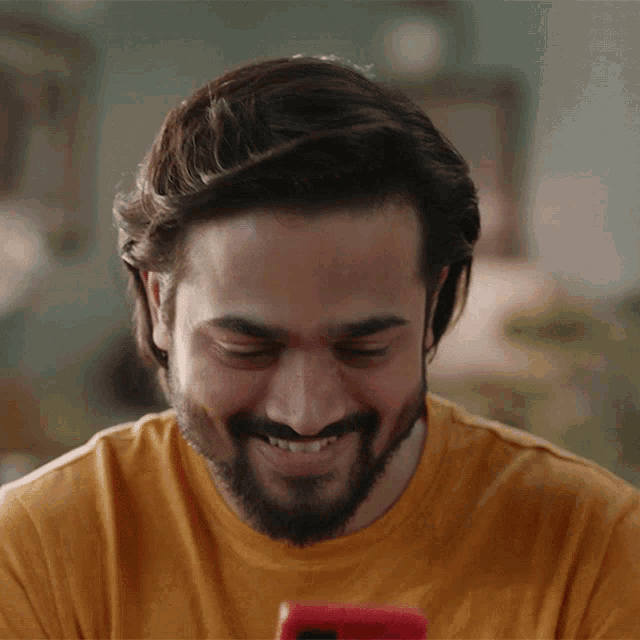 a man with a beard is smiling while looking at a phone
