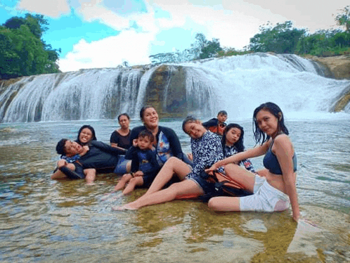 a group of people are posing for a picture in the water near a waterfall .