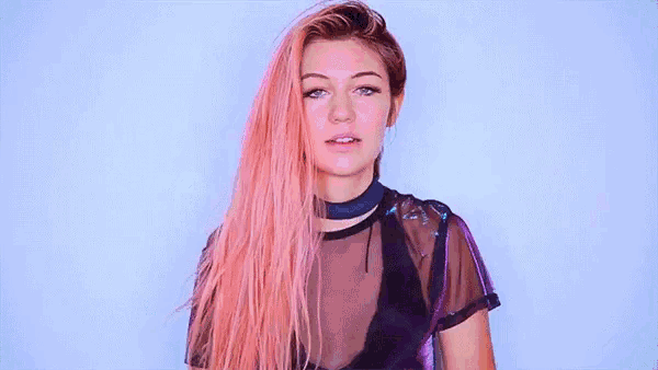a woman with pink hair is wearing a choker and a sheer top .