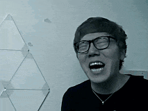 a man wearing glasses and a black shirt is laughing with his mouth open