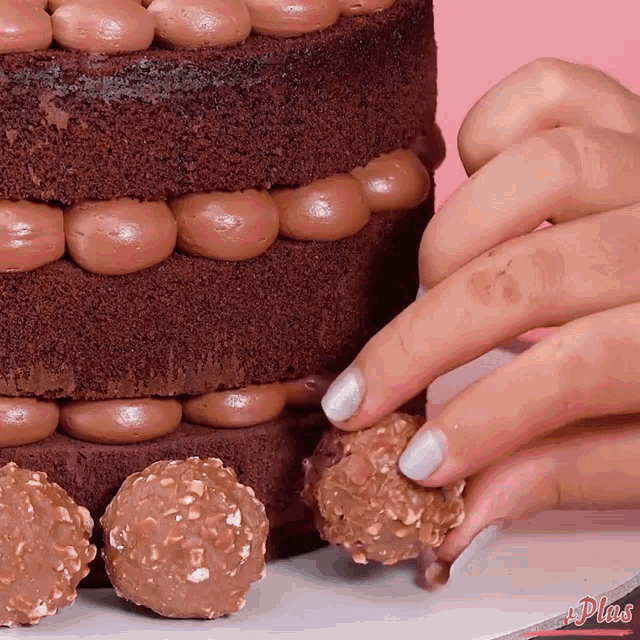 a close up of a person 's hand reaching for a chocolate cake covered in chocolate frosting