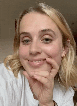 a woman with blonde hair is smiling with her hand on her chin .