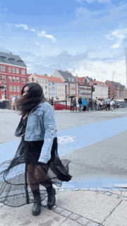 a woman wearing a denim jacket and a black skirt is walking down a street