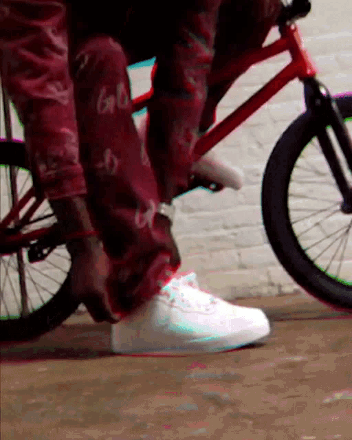a person wearing red pants and white sneakers is riding a red bike