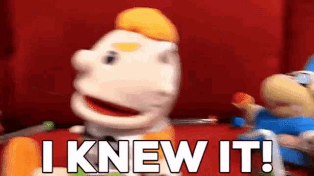 a puppet says i knew it in front of a red wall