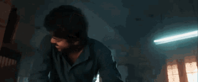 a man with a beard is standing in a dark room with a blue light coming from the ceiling .