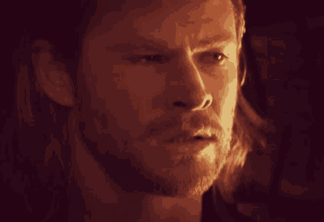 a close up of a man 's face with a beard in a dark room .
