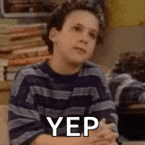 a young boy in a striped sweater is sitting at a table with his hands folded and the word yep on his face .