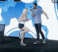a man singing into a microphone while a woman stands on one leg
