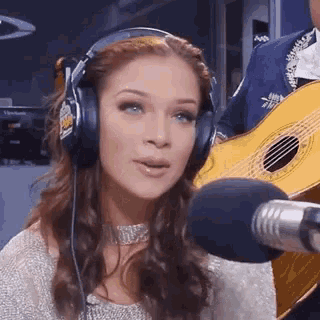 a woman is wearing headphones and holding a guitar in front of a microphone .