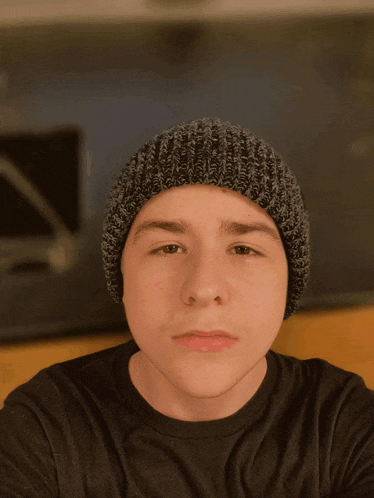 a young man wearing a black shirt and a grey beanie looks at the camera