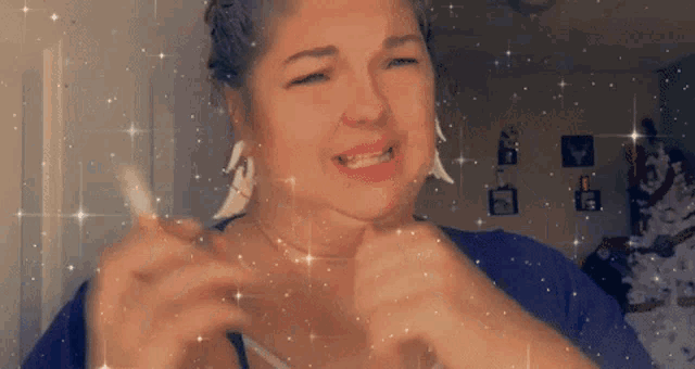 a woman wearing a purple shirt and white earrings is making a funny face with her hands .