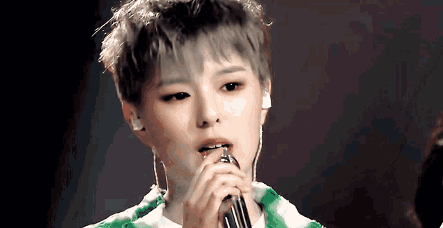 a woman singing into a microphone with a green plaid shirt on