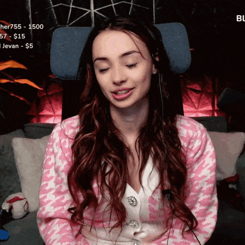 a woman in a pink and white sweater sits on a couch with her eyes closed