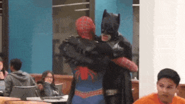 a man in a spiderman costume and a man in a batman costume are hugging each other in a room .
