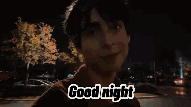 a young man is walking down a street at night and smiling while saying good night .