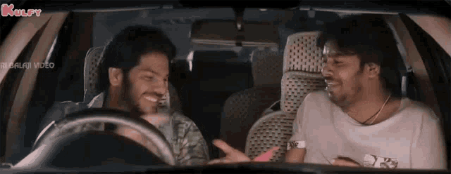 two men are sitting in the back seat of a car and talking to each other .