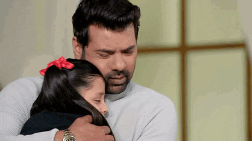 a man is hugging a little girl with a red bow on her hair .