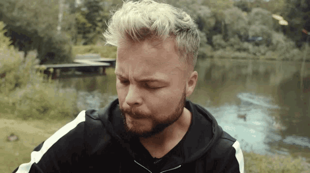 a man with blonde hair and a beard is standing in front of a body of water