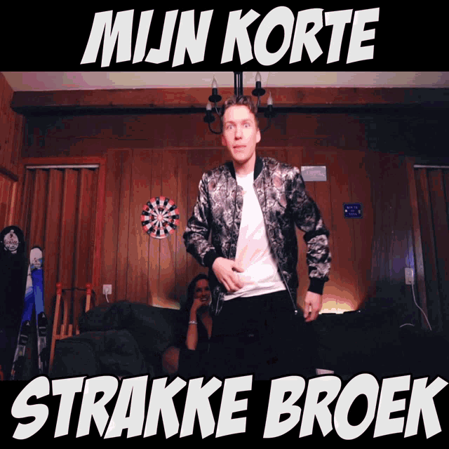 a man in a bomber jacket stands in front of a dart board with the words mijn korte strakke broek written on it
