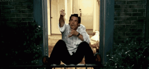 a man is sitting on a balcony looking out of a window at night .