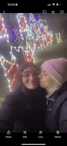 a woman kissing another woman on the cheek in front of a house with christmas lights