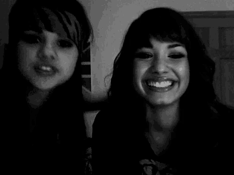 a black and white photo of two women smiling for the camera . one of the women is wearing a zebra print bandana .