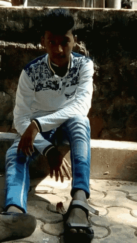a young man in a white shirt sits on a sidewalk