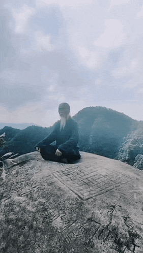 a man sits in a lotus position on a rock
