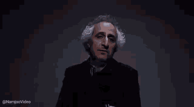 a man with gray hair and a beard is standing in a dark room and making a funny face .
