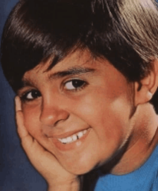 a young boy smiles with his hand on his chin
