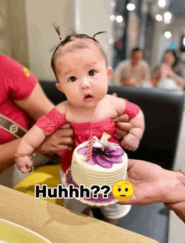 a baby is being held by a person holding a small cake with a candle and the words huhhh on it